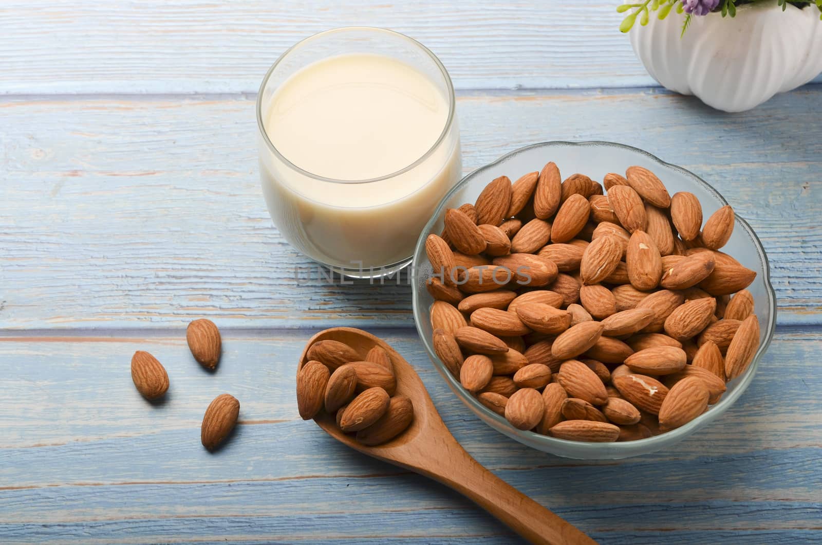 Close up view of healthy almond milk in drinking glass with seed in bowl on wooden background. Selective focus.