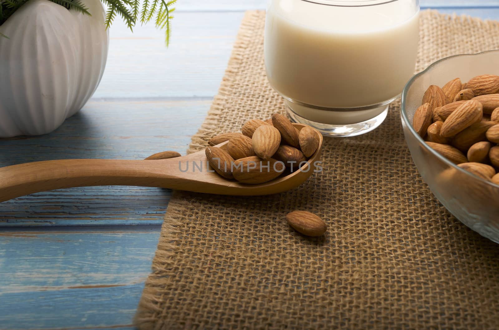 Close up view of healthy almond milk in drinking glass with seed in bowl on wooden background. Selective focus.