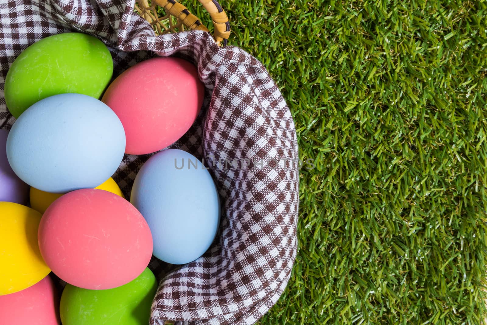 Group of colorful eggs in a basket placed on green grass field.
