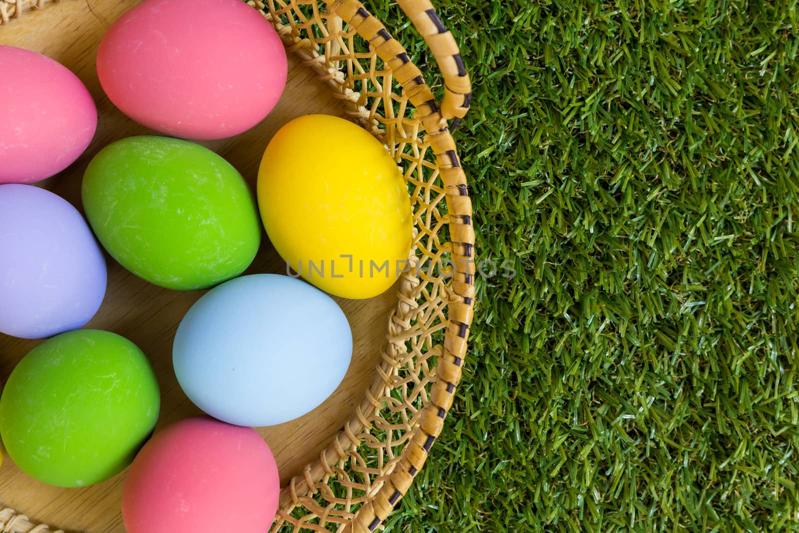 Group of colorful eggs in a basket placed on green grass field.