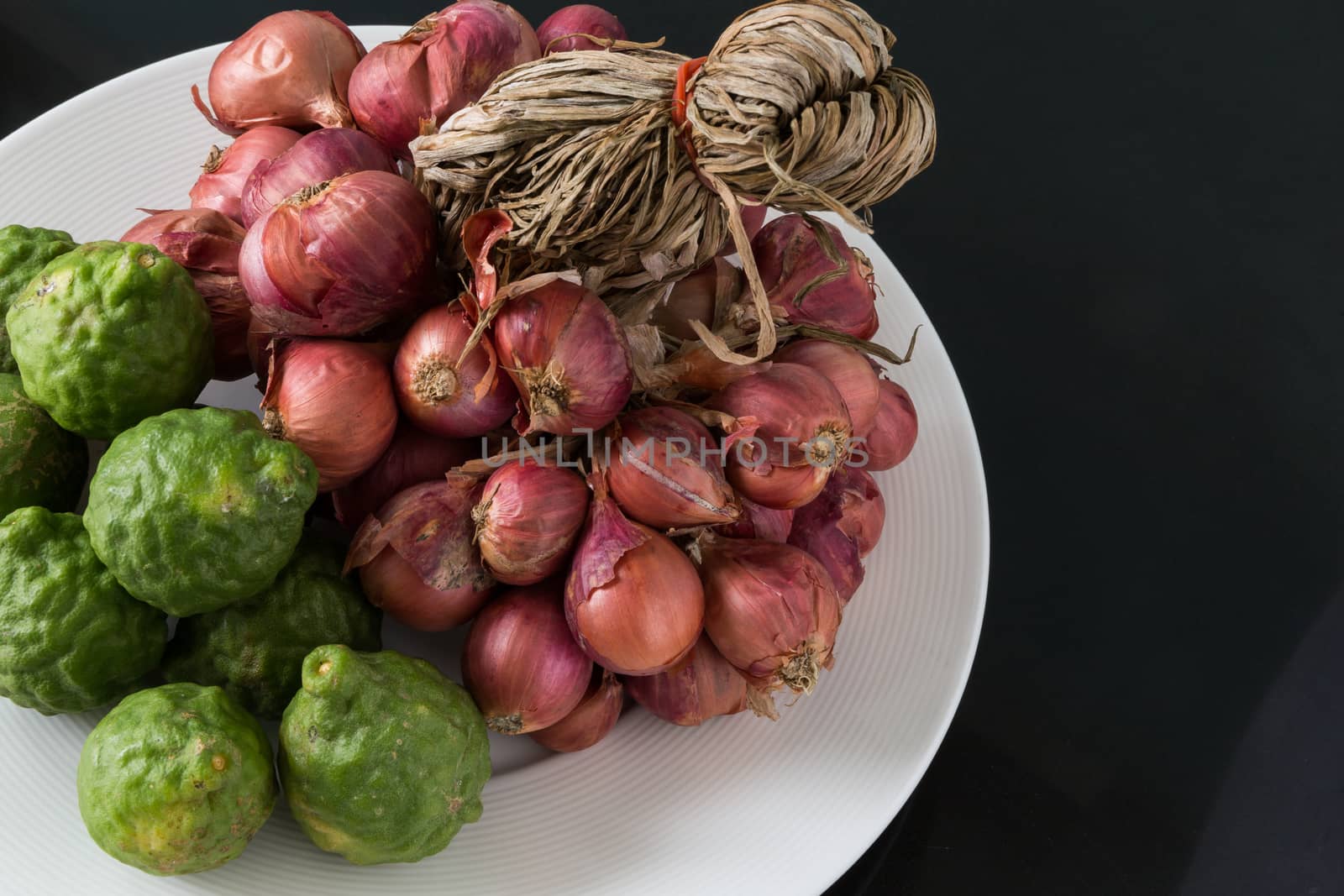 Raw bergamot and shallot in a plate on black background
