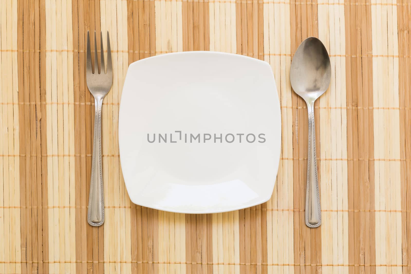 Empty plate with spoon and fork on table background.