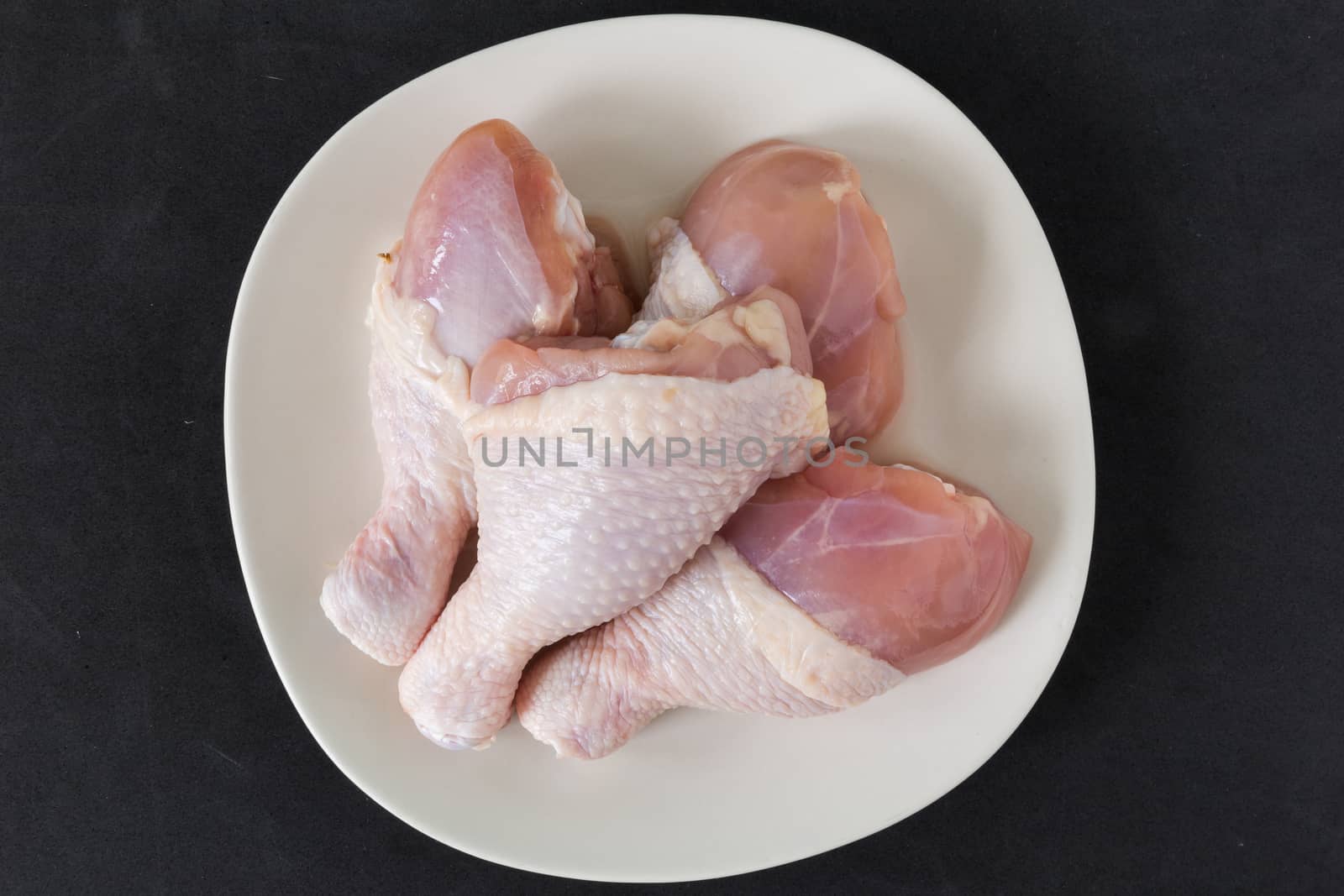 Fresh chicken legs on a plate on black background.
