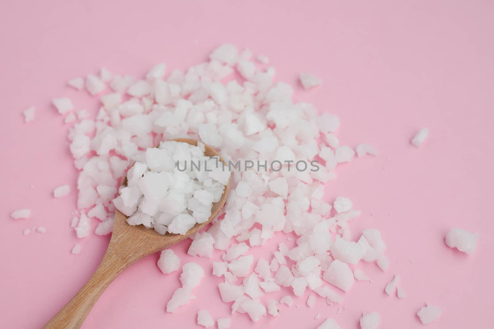 Sea salt in a wooden spoon on pink background for seasoning or preserving food
