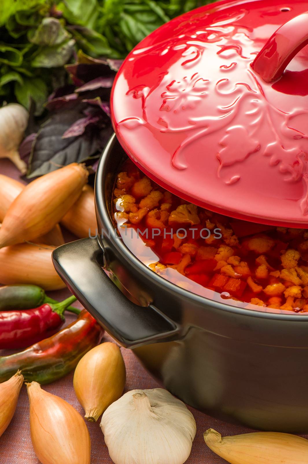 Cold vegetable soup in a black ceramic pot with red cover