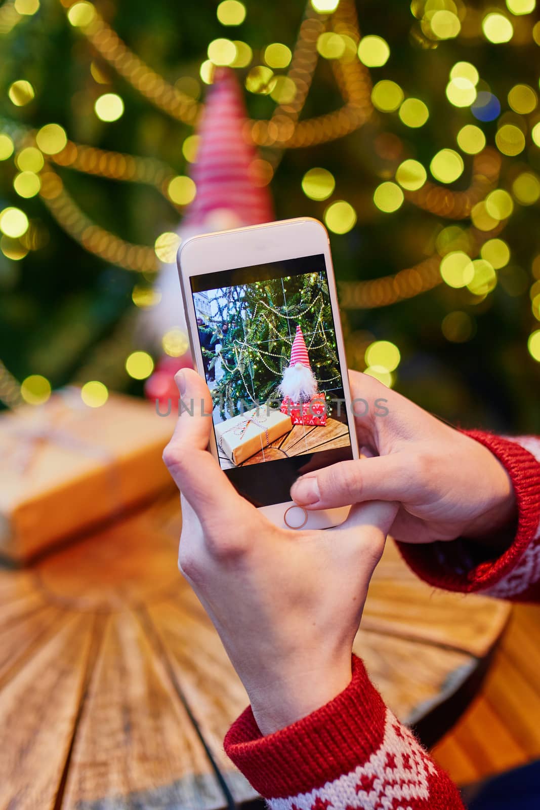 Woman taking photo of her coffee cup and Christmas present in cafe decorated for seasonal holidays