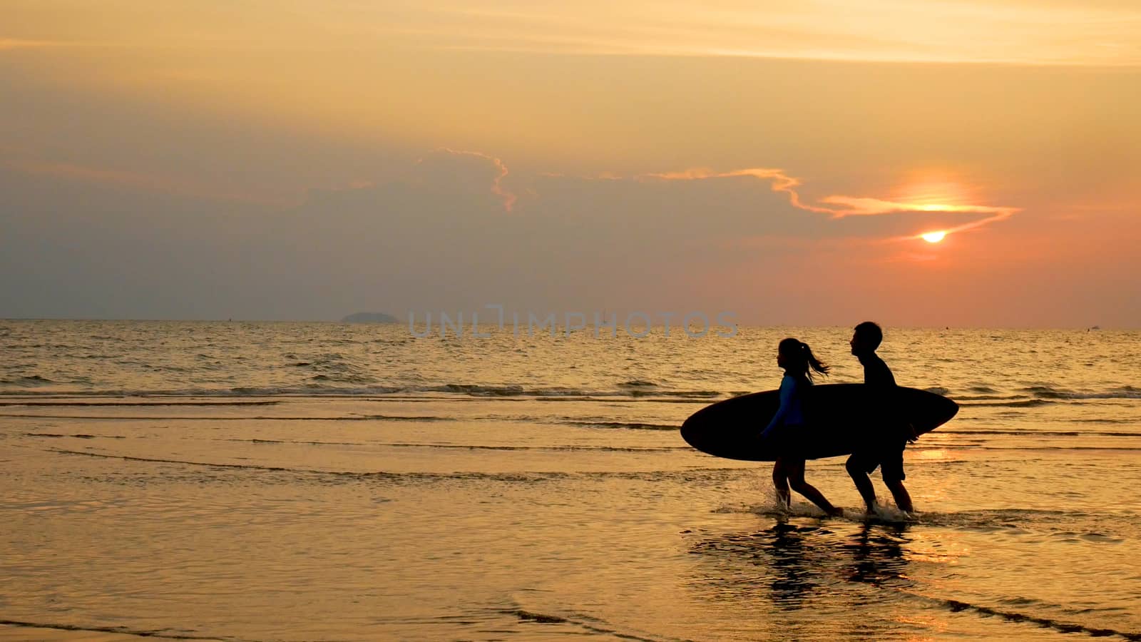 silhouette of young happy people ,surf man and girl running with long surf boards at sunset tropical beach. surfer on the beach in sea shore at sunset time with beautiful light. water sport activity by asiandelight