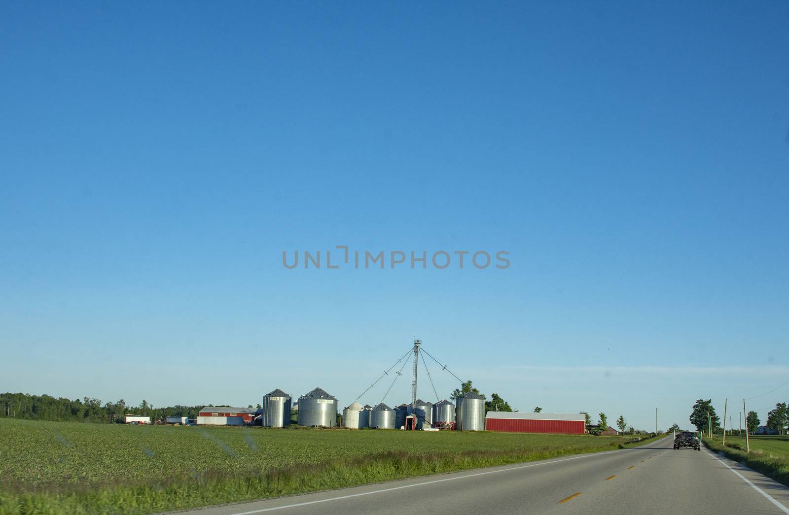 Farm buildings at the end of a large field that stretches along the road