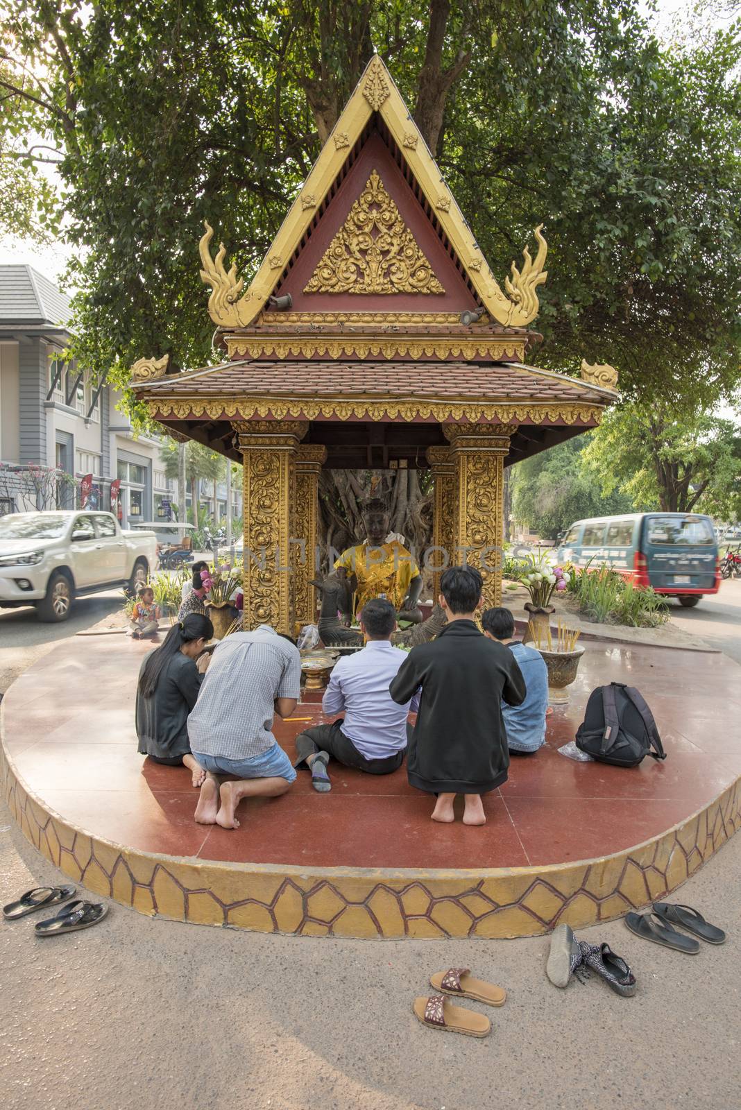 Cambodian Worshippers praying in front of King Master Statue located under a tree and in the Middle of the road, Siem Reap, Cambodia