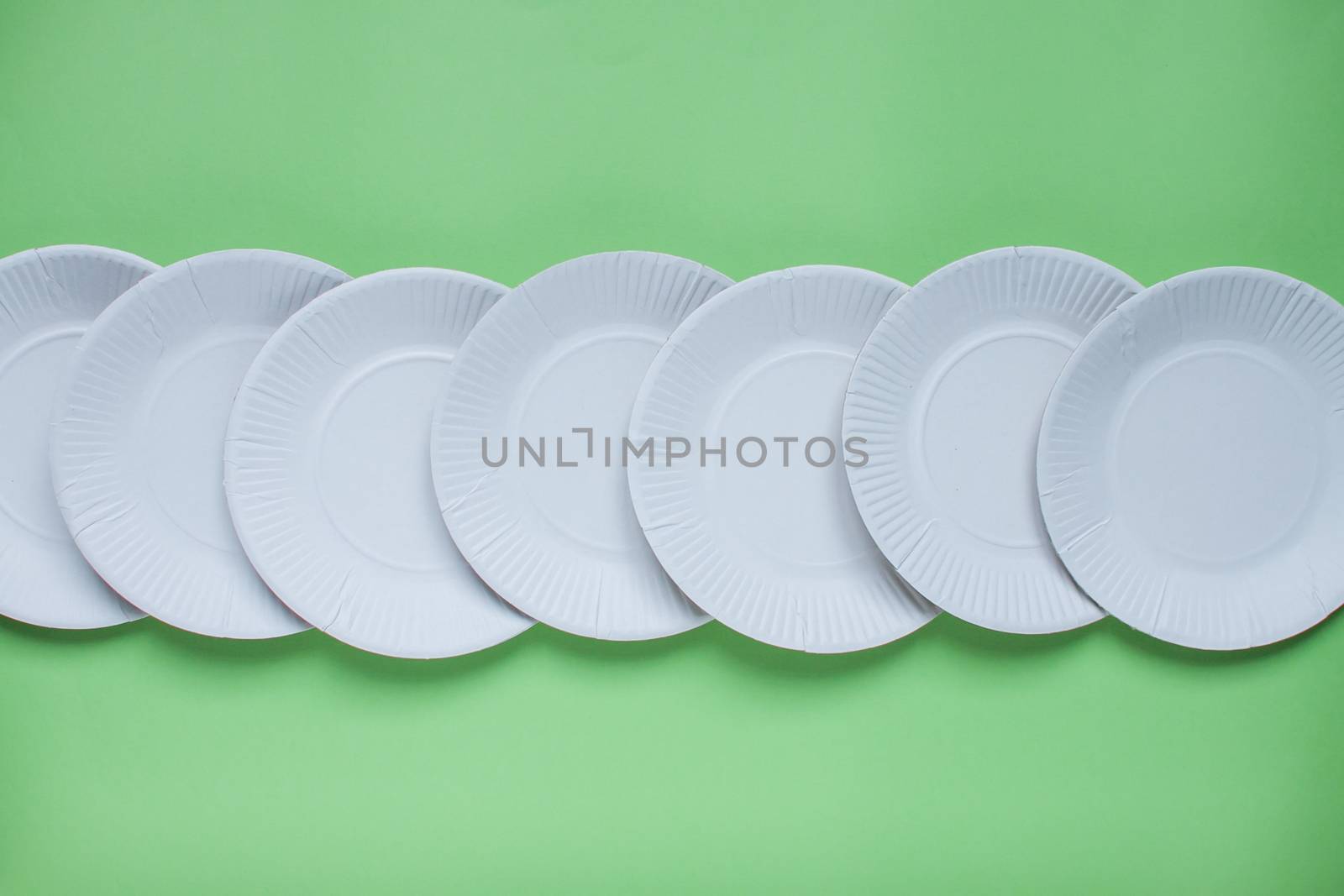 The layout on a green background from paper disposable plates. Caring for the environment. Recycling and sorting of garbage. Disposable tableware. Environmental pollution. by malyshkamju