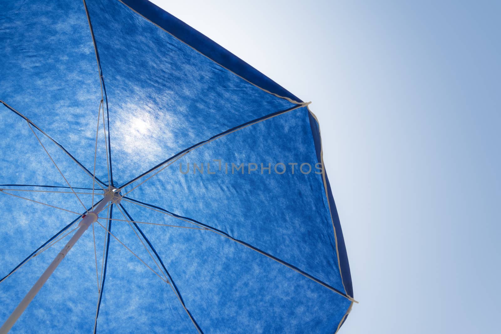 Blue beach parasol against blue sunny sky and in contre-jour