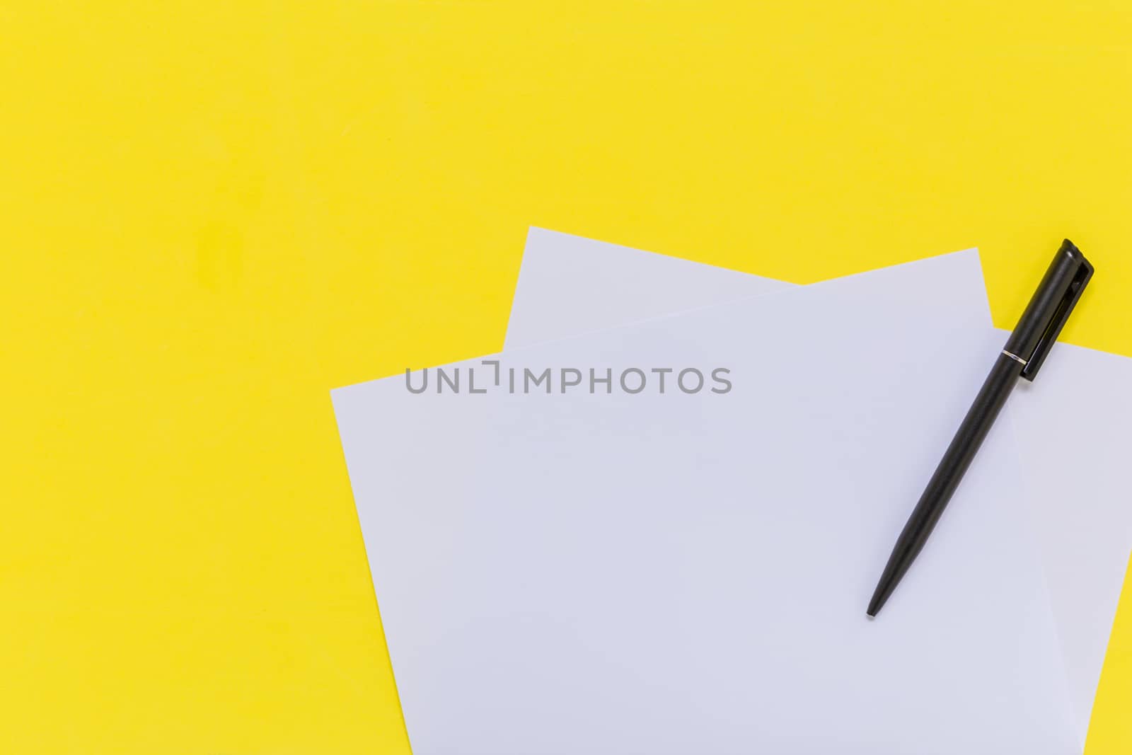 Sheets of white blank paper with pen on yellow background.