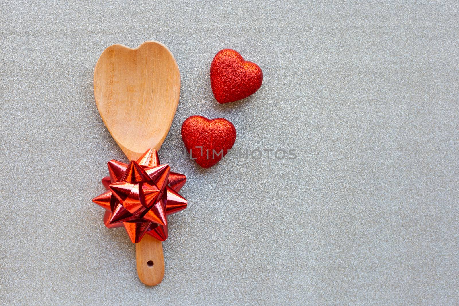The red heart shapes and wooden spoon with red bow on silver glitter paper background in love concept for valentines day.