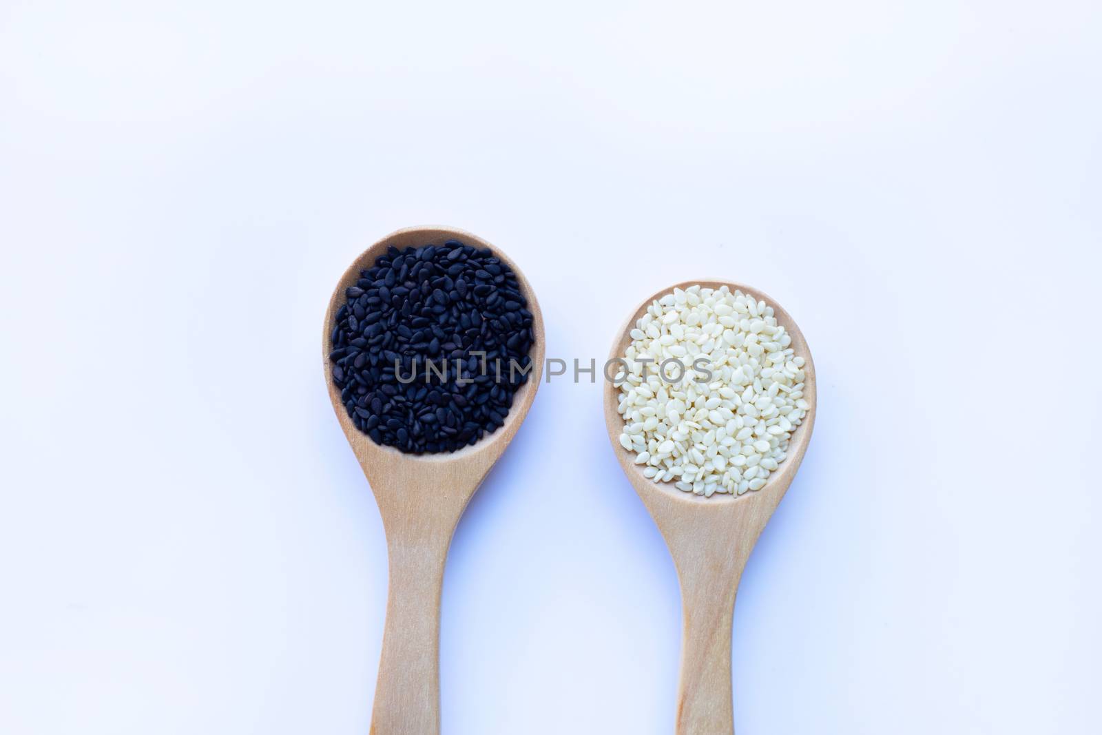 Black and white sesame seeds on wooden spoon, white background. Copy space