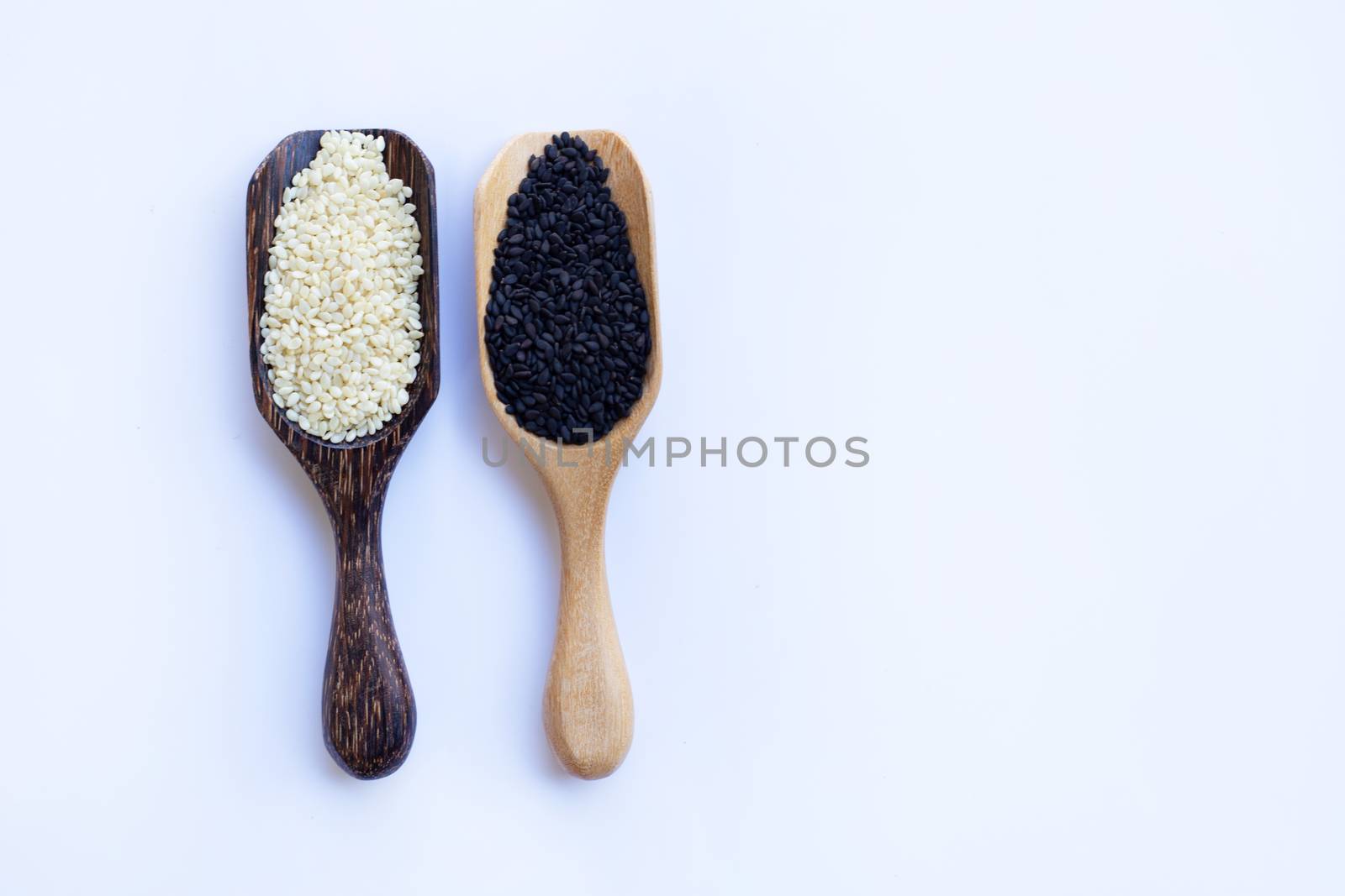 Black and white sesame seeds on wooden spoon, white background. Copy space