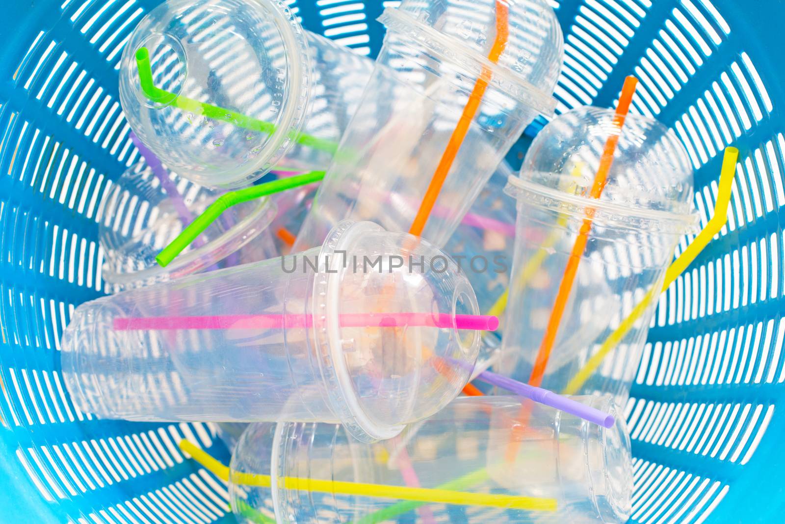 Plastic cups with straws in waste basket.
