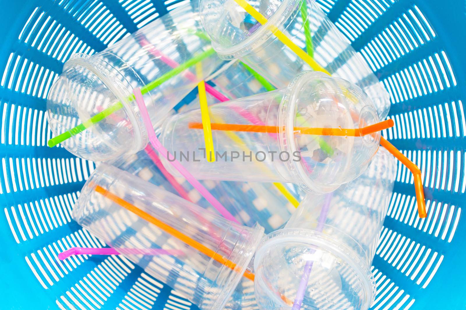 Plastic cups with straws in waste basket.