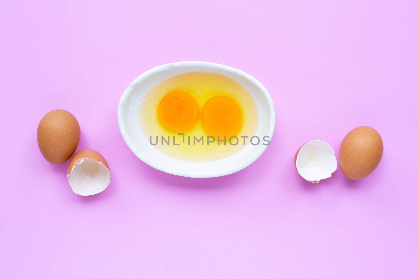 Two egg yolk and white in a bowl on pink background.  Top view