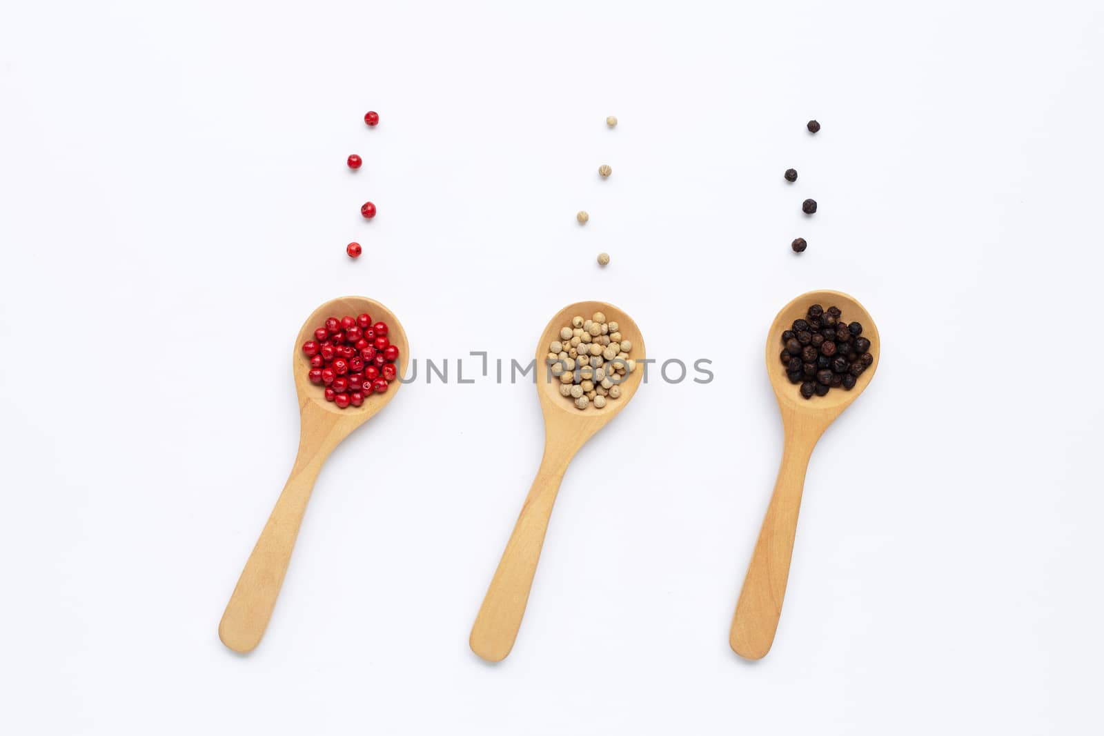 Red, white and black peppercorns with wooden spoon on white background.
