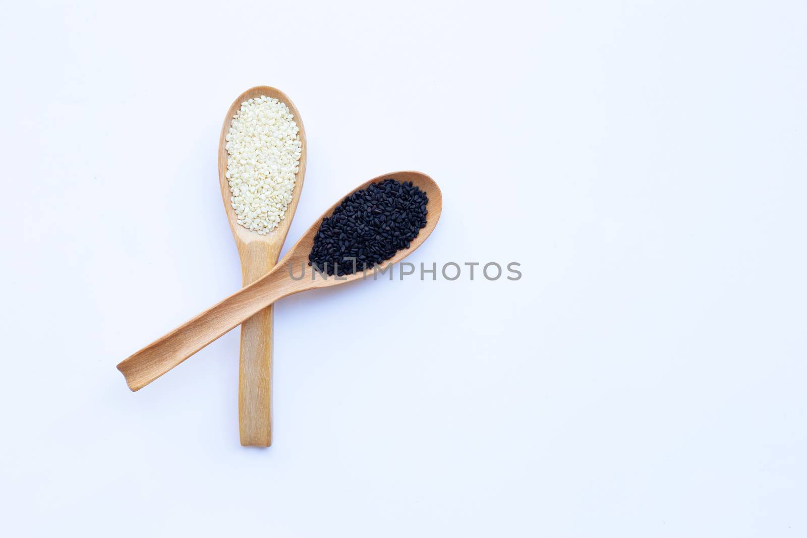 Black and white sesame seeds on wooden spoon, white background. Copy space