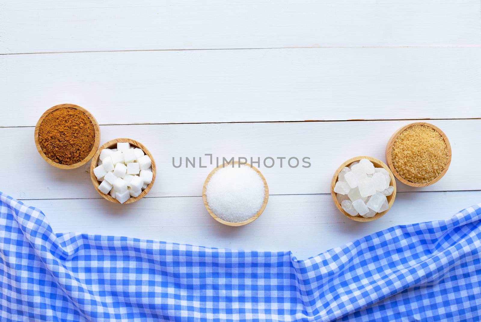 Various types of sugar on white wooden background.