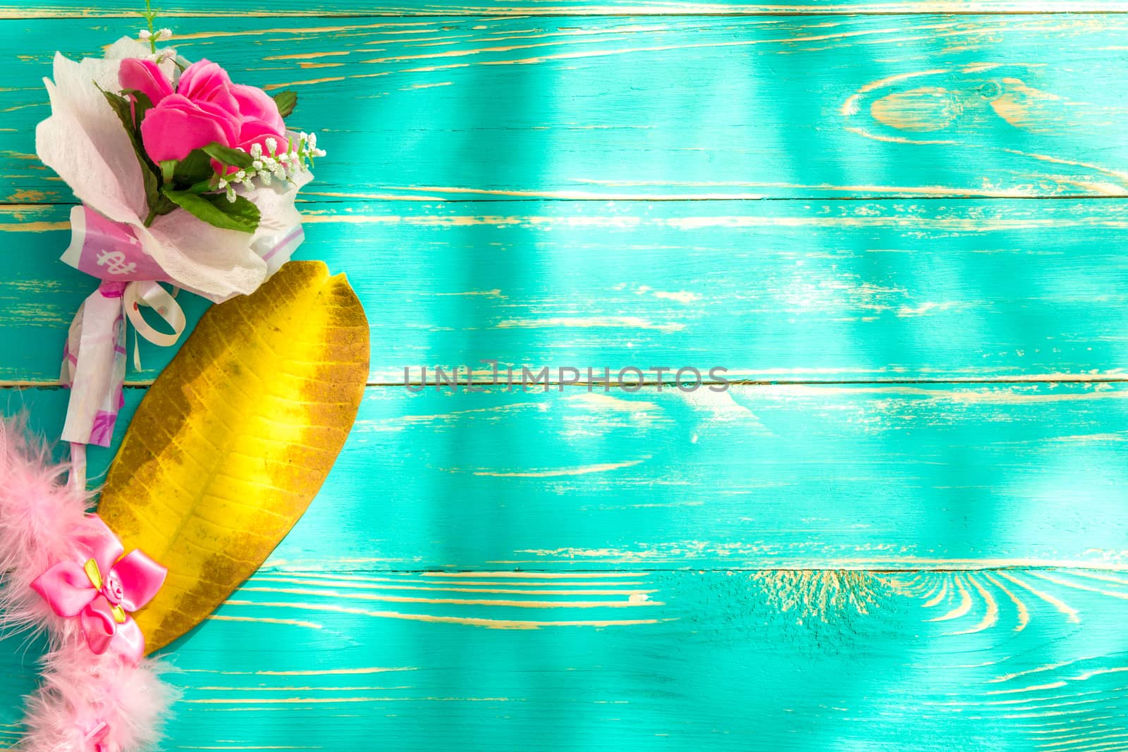 Flower put aside yellow leaf on blue wooden background.