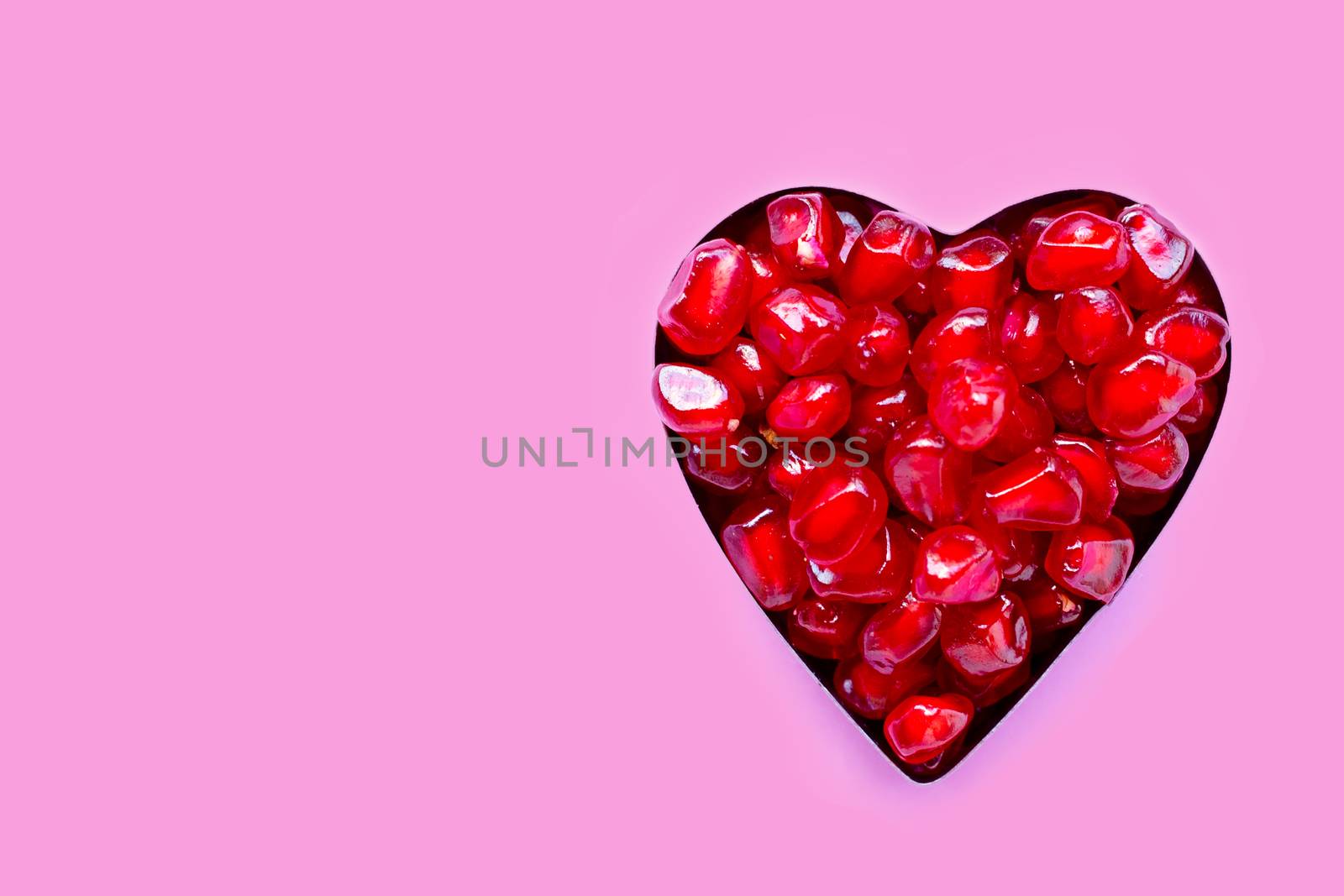 Pomegranate  seeds in steel heart shaped mold on pink background.
