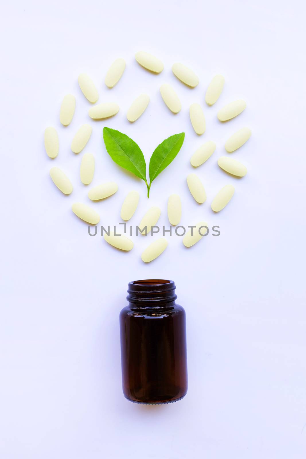 Vitamin C bottle and pills with green leavs on white background.