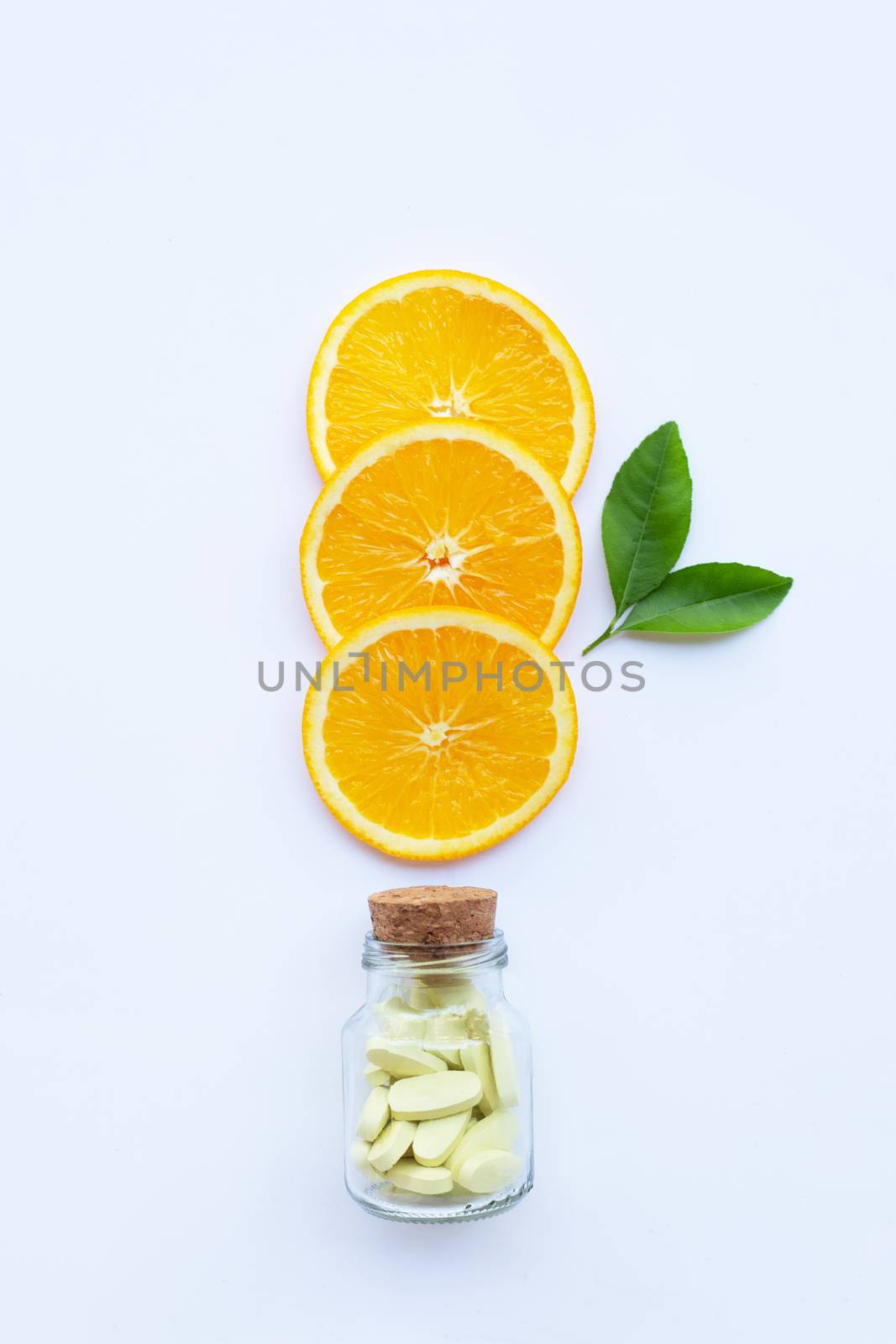 Vitamin C bottle and pills with orange fruit on white background.