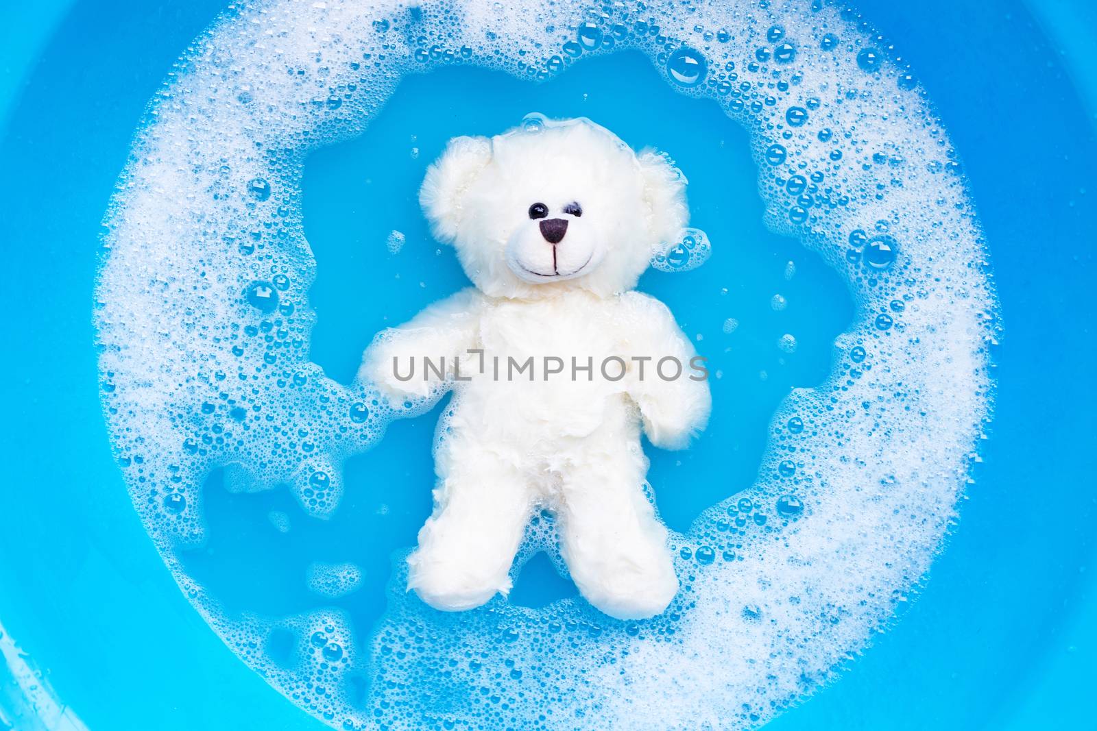 Soak toy bear in laundry detergent water dissolution before wash by Bowonpat
