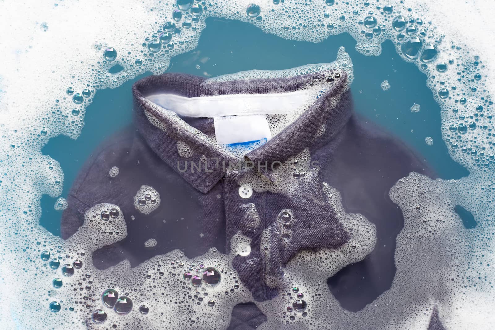 Grey polo shirt soak in powder detergent water dissolution, washing cloth. Laundry concept