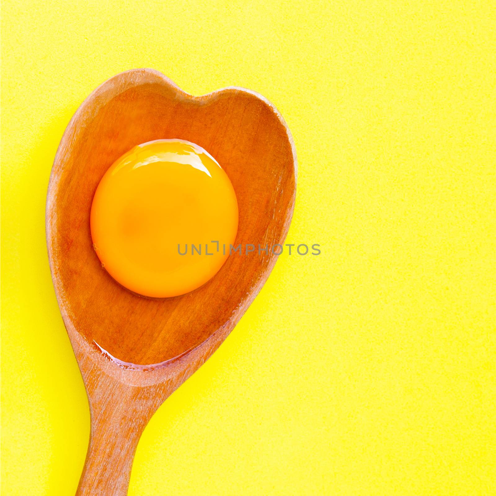 Egg yolk and white on  wooden spoon heart shape on yellow background. Top view