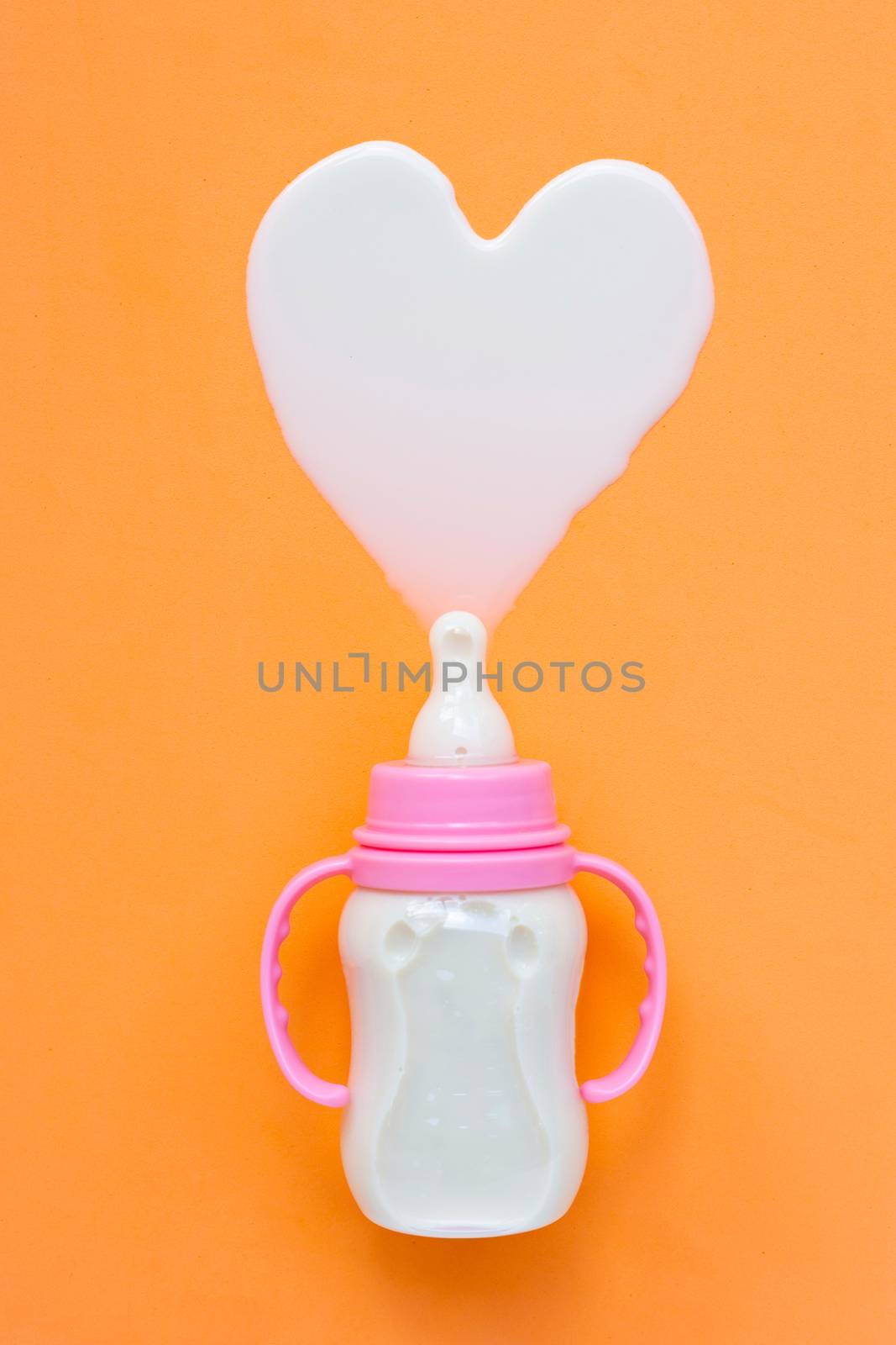 Bottle of milk for baby on orange background. Milk heart shape, Top view