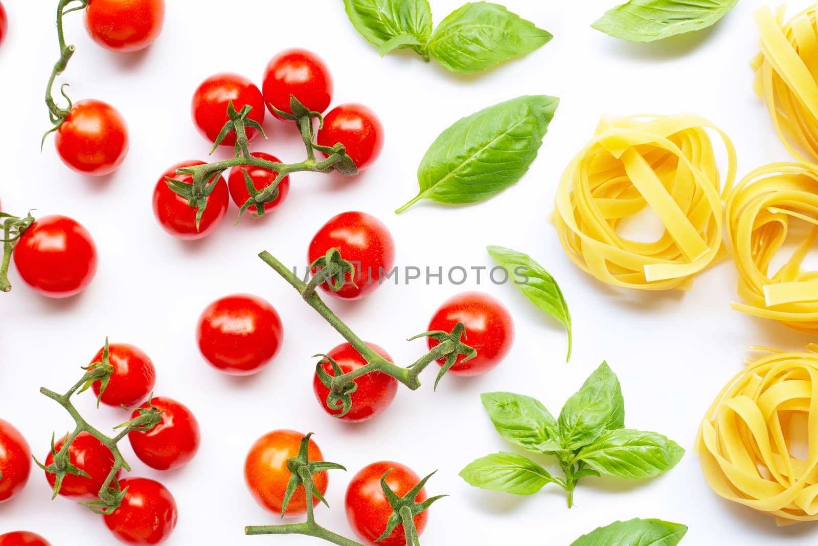 Cherry tomatoes with  basil leaves  and uncooked pasta tagliatelle nest on white background. Italian food concept