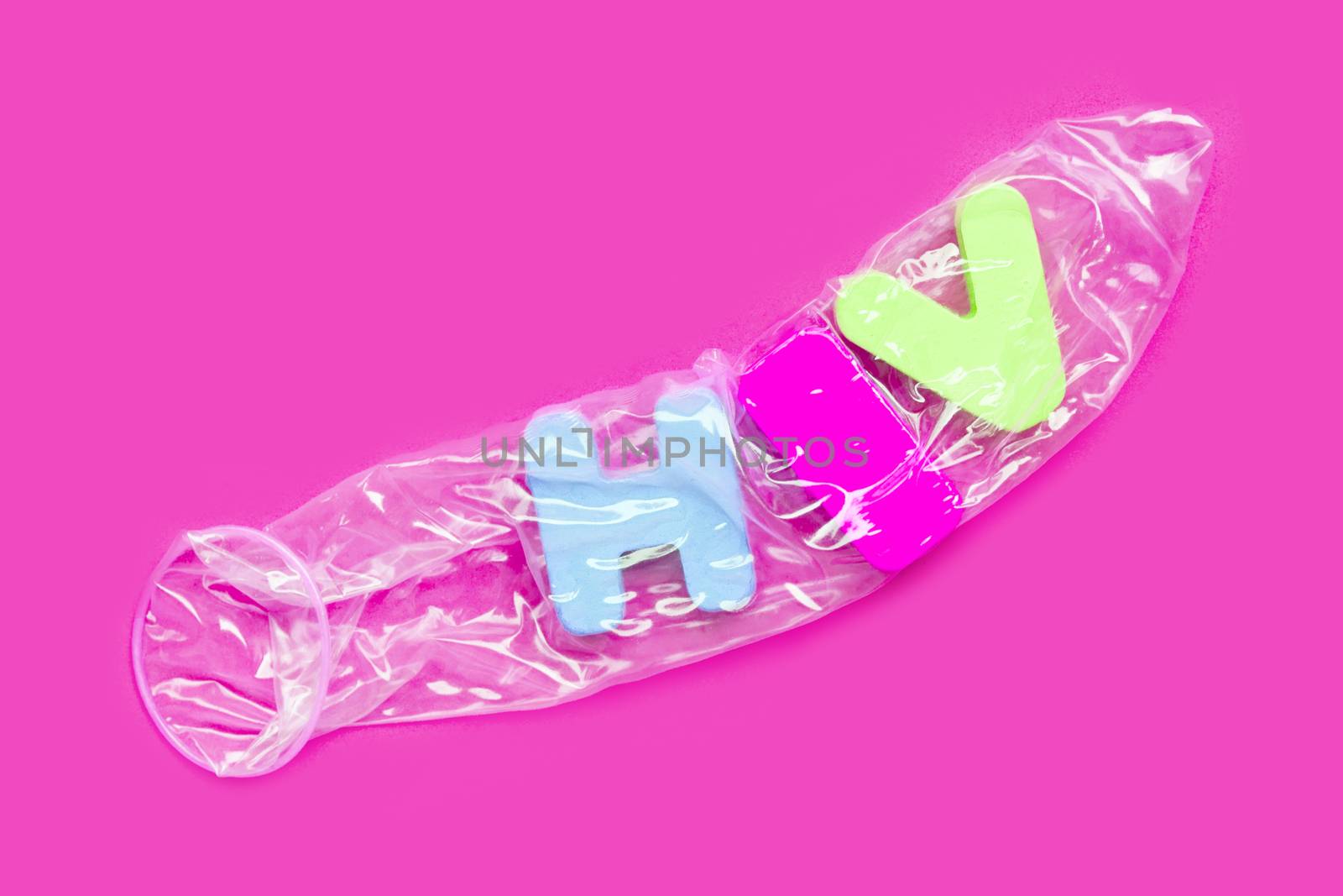 Condom with "HIV" wooden alphabet on pink background.