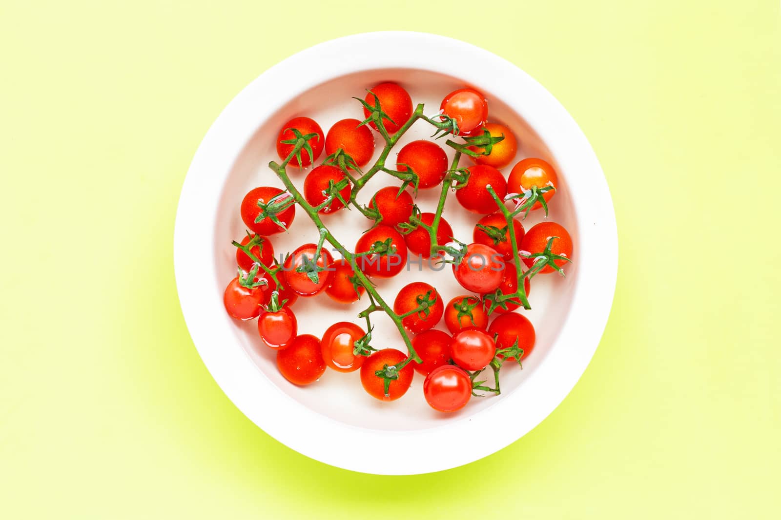 Fresh tomatoes in a bowl of water on green background.  Washing vegetables  concept
