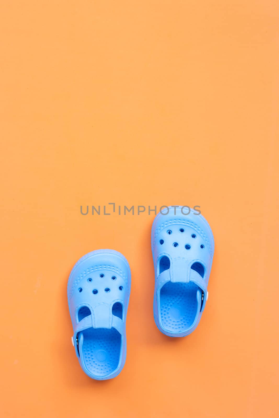 Blue children's rubber sandals on orange background. Top view and copy space