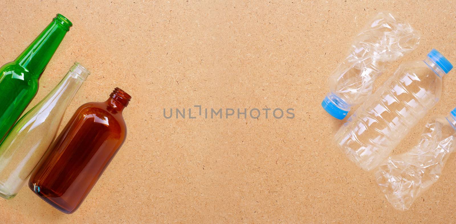 Glass bottles with plastic bottles on plywood background. Copy space
