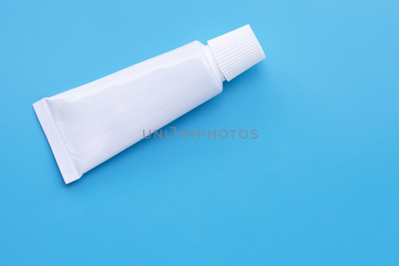 Small white toothpaste tube on blue background. by Bowonpat