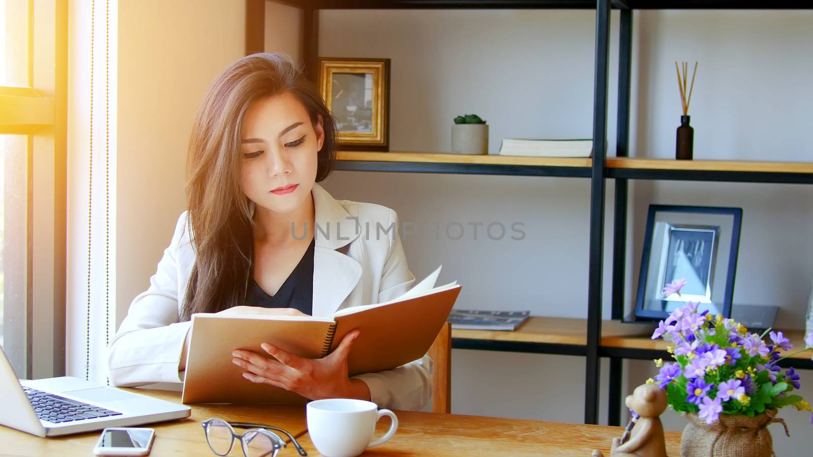 startup business in Asia concept. young Asian business woman reading book with thinking face working with laptop at workplace, film effect and sun flare effect.