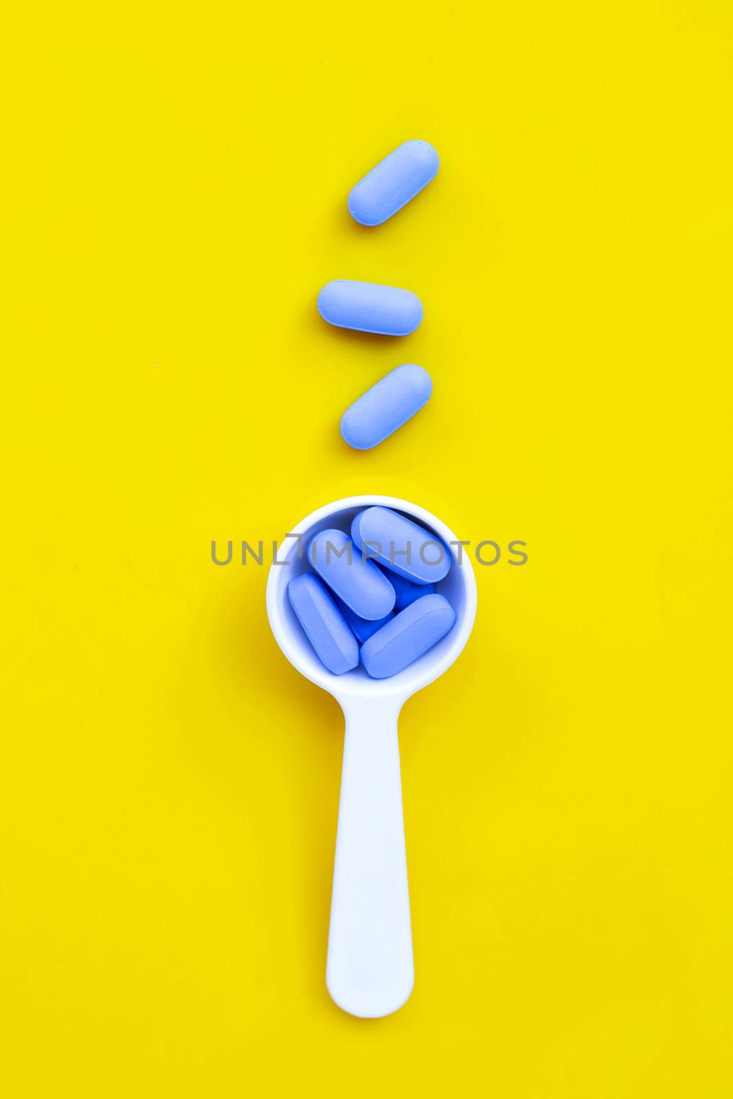 Medical blue pills with white plastic spoon on yellow background. Top view