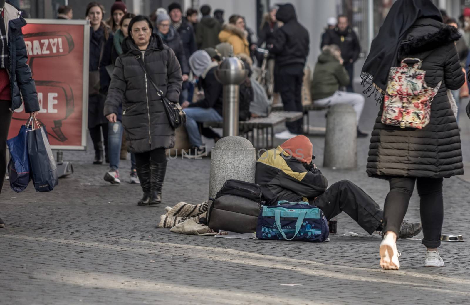 Brunswick, Lower Saxony, Germany, December 7th 2017: Freezing and tired poor beggar in the pedestrian zone in front of the Christmas market of Brunswick.