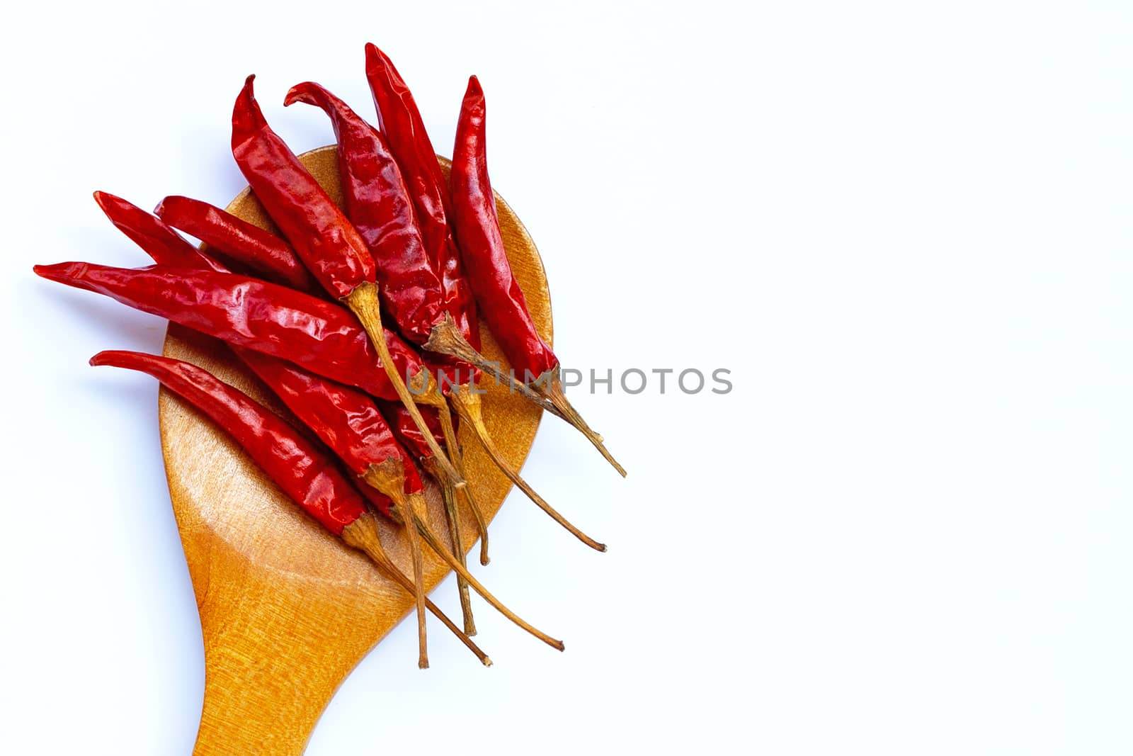 Dry red hot chili peppers on wooden spoon on white background. Copy space
