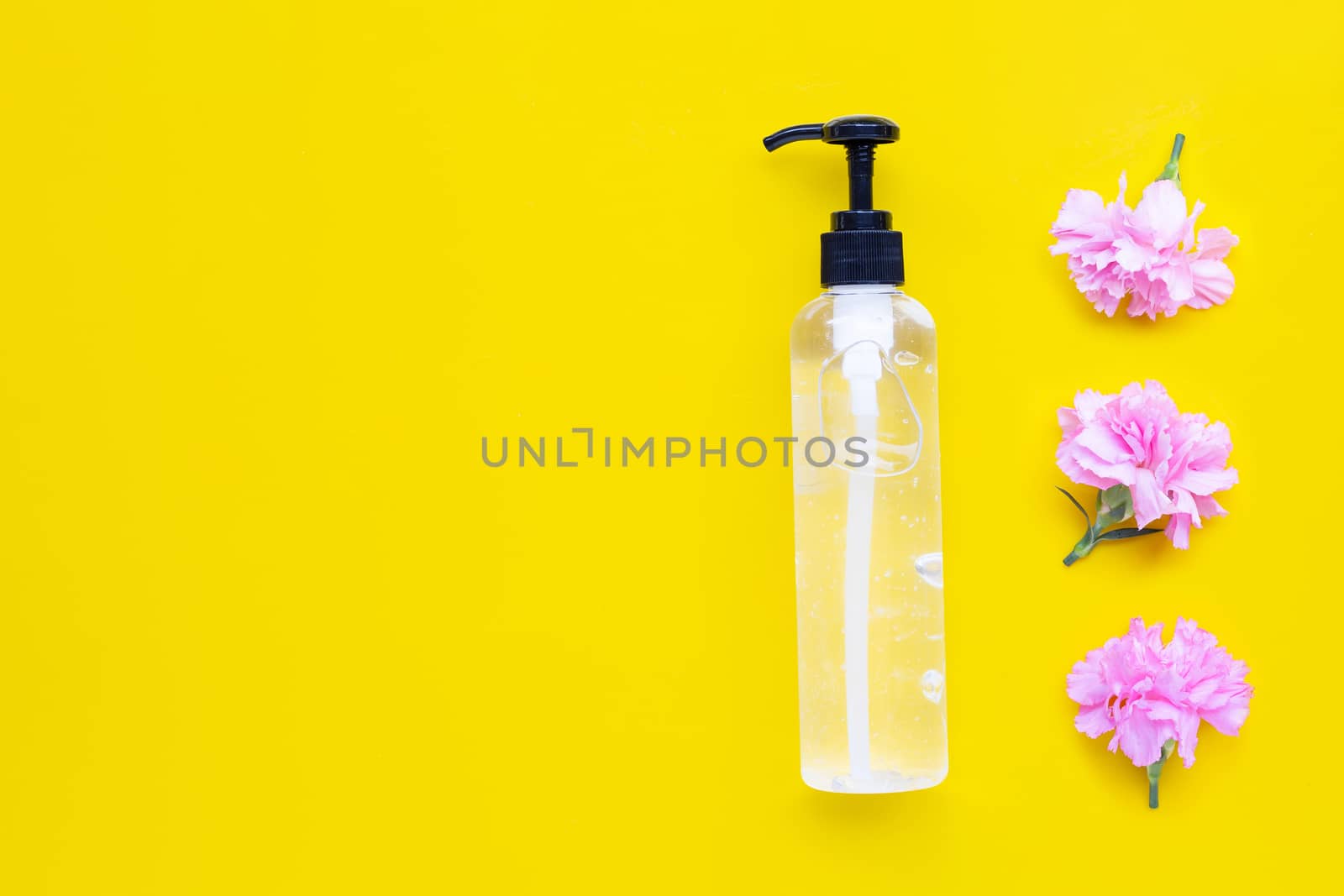 Alcohol hand sanitizer gel in pump bottle with pink carnation flower on yellow background. Hand hygiene corona virus protection concept.