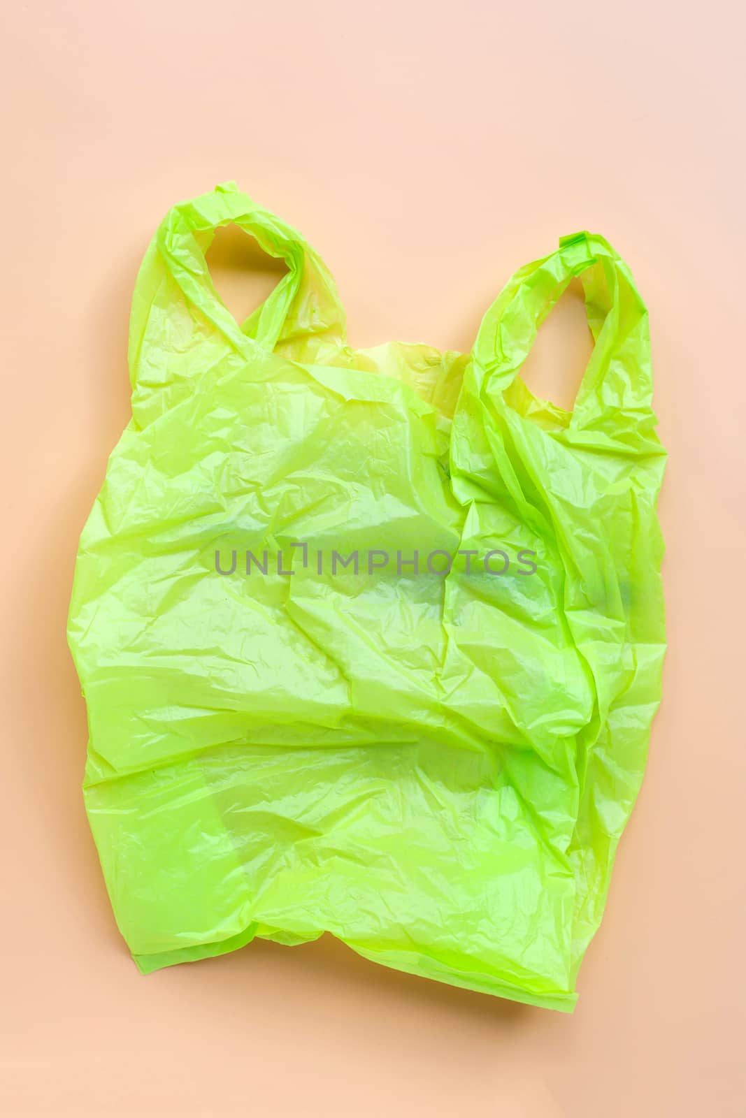Green plastic bag on yellow background. Environment pollution concept. Top view