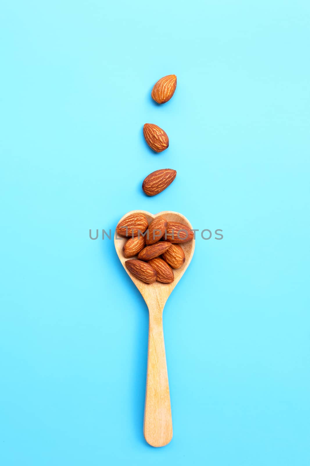 Almonds on heart shape wooden spoon on blue background. Top view