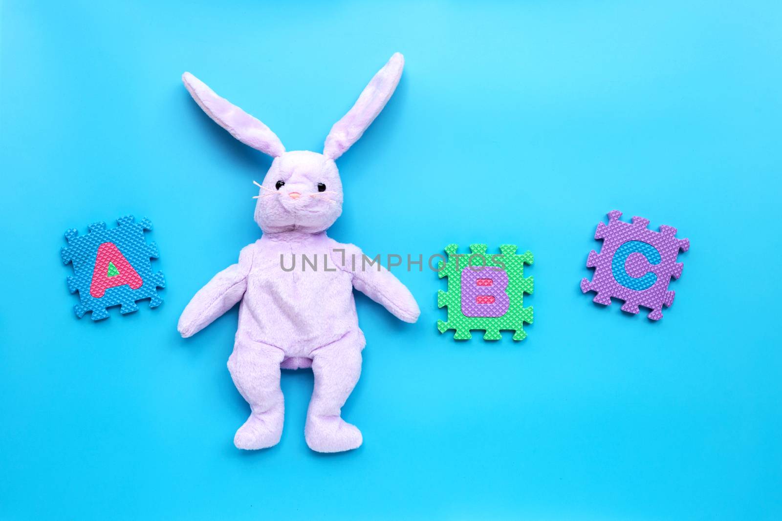 Rabbit toy with english alphabet puzzle on blue background. Education concept, Copy space