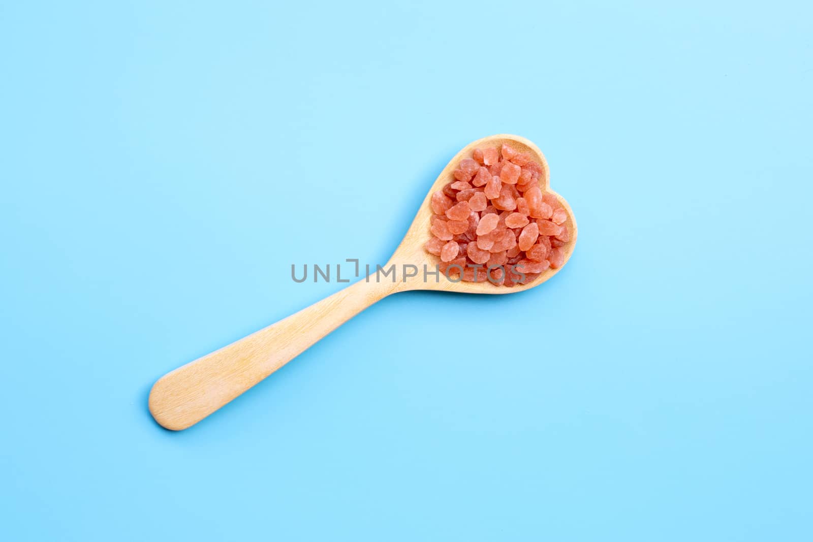Pink himalayan salt in heart shape wooden spoon on blue background. Copy space