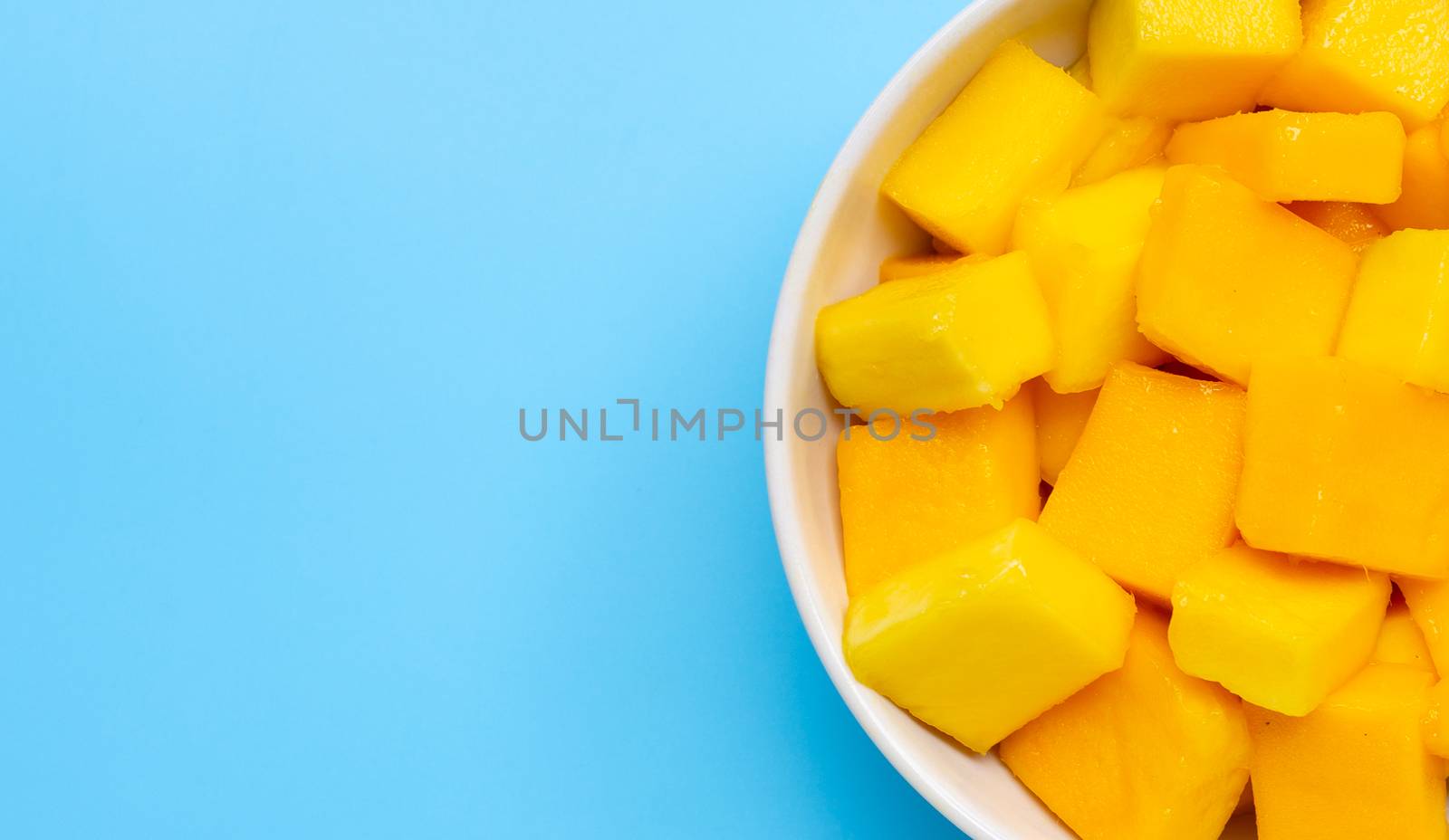 Tropical fruit, Mango cube slices in white bowl on blue background. Copy space