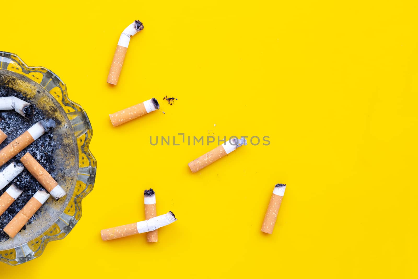 Ashtray and cigarettes on yellow background. Copy space